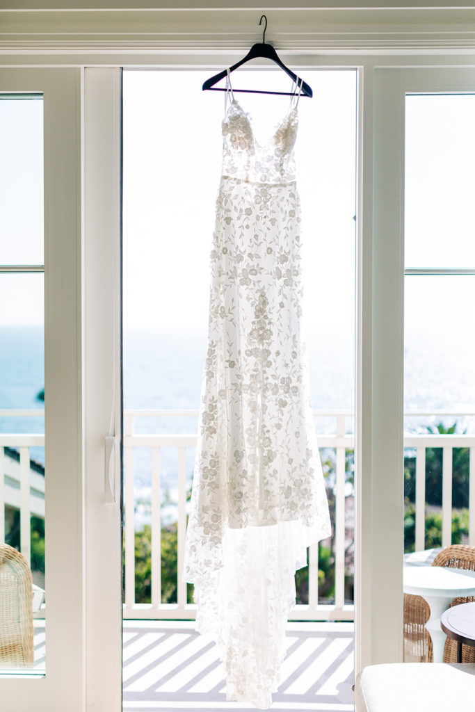 Crystal Cove Micro Wedding in Orange County; wedding dress hanging in a window with the ocean in the background