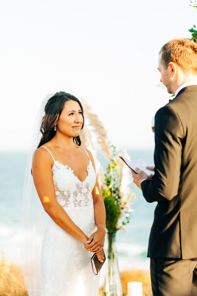Crystal Cove Micro Wedding in Orange County; bride smiling as the groom reads his vows at their wedding