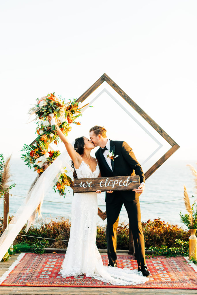 Crystal Cove Micro Wedding in Orange County; bride and groom holding a sign that says "we eloped"