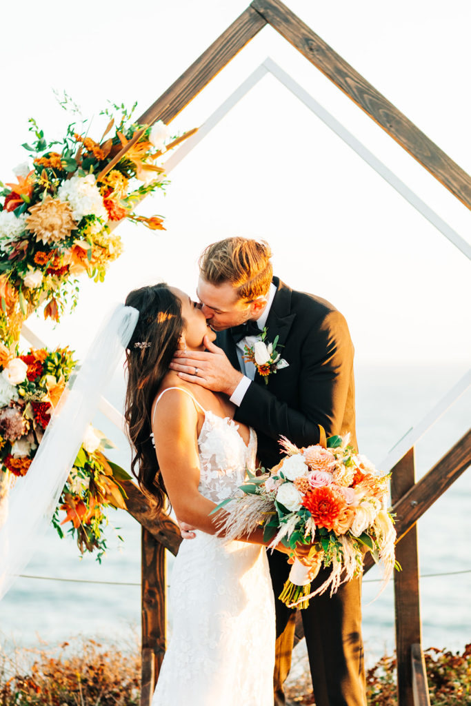 Crystal Cove Micro Wedding in Orange County; groom standing behind his bride and kissing her