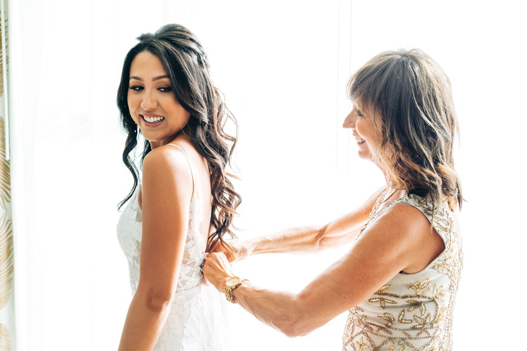 Crystal Cove Micro Wedding in Orange County; bride's mom helping the bride zip up her wedding dress on her wedding day