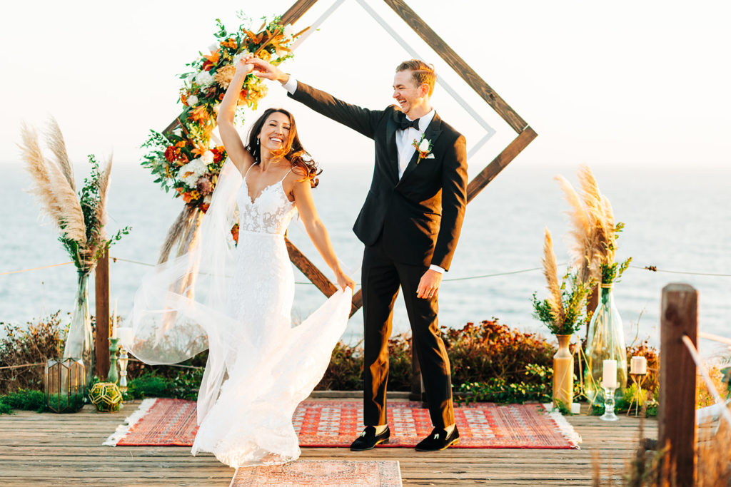 Crystal Cove Micro Wedding in Orange County; bride and groom smiling as the groom spins the bride while dancing