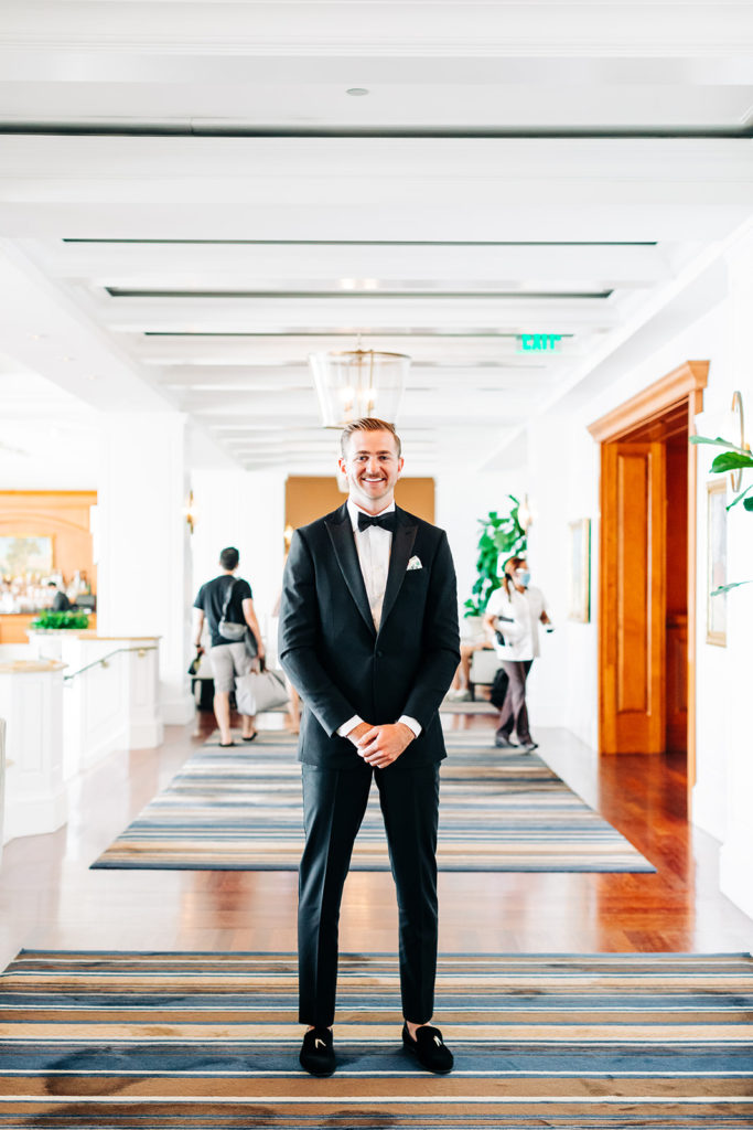 Crystal Cove Micro Wedding in Orange County; portrait of a groom on his wedding day, he is a wearing a black suit and standing in a hotel lobby