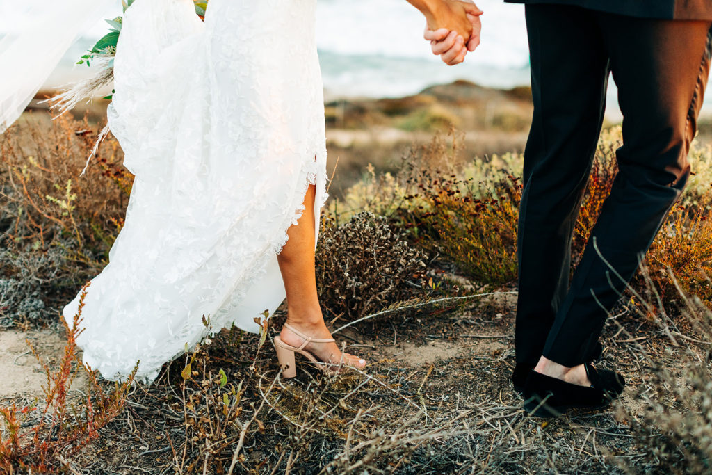 Crystal Cove Micro Wedding in Orange County; feet of a bride and groom walking through brush