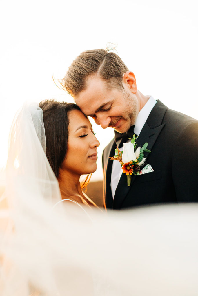 Crystal Cove Micro Wedding in Orange County; bride and groom with their faces close together as the bride's veil blows in front of them