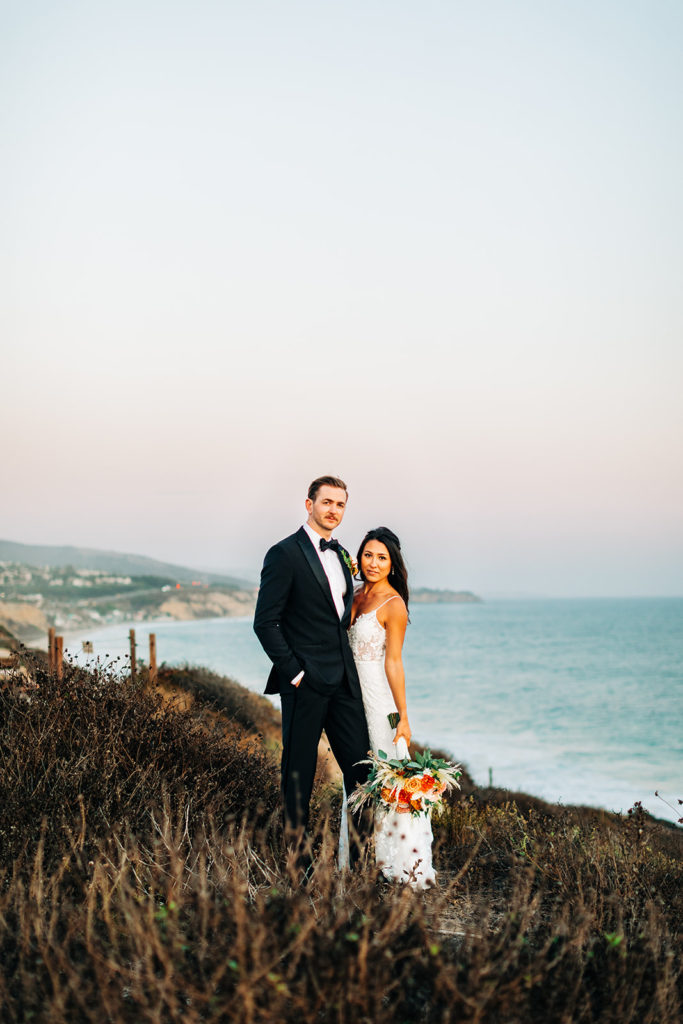 Crystal Cove Micro Wedding in Orange County; bride and groom looking at the camera with a beautiful sunset behind them
