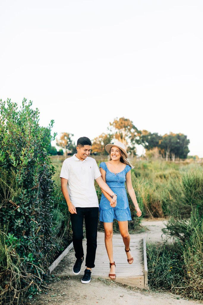 Newport Back Bay Engagement Photos; man and woman couple walking while holding hands. they are surrounded by greenery