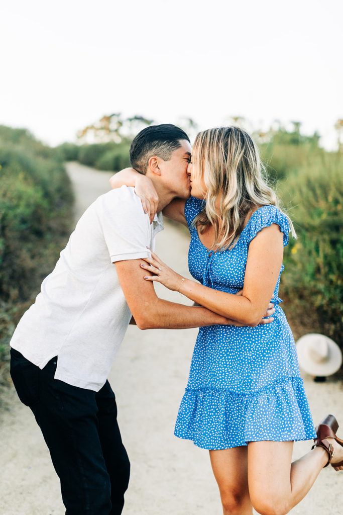 Newport Back Bay Engagement Photos; a man and woman kissing, the woman has on a blue dress with white dots