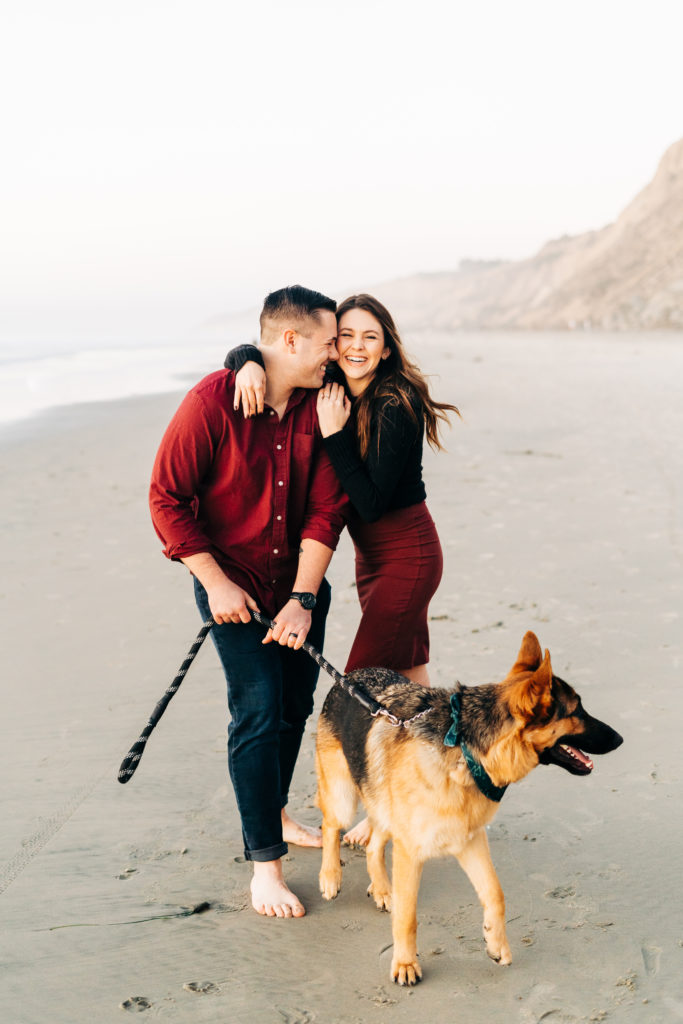 black's beach engagement photos; san diego wedding photographer; a husband and wife and their dog, they are smiling and laughing with each other
