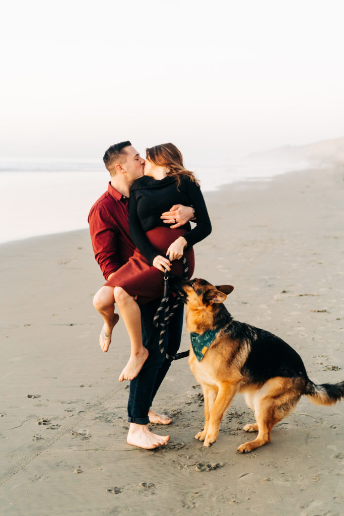 black's beach engagement photos; san diego wedding photographer; a husband holding his wife, they are kissing. their dog is with them.