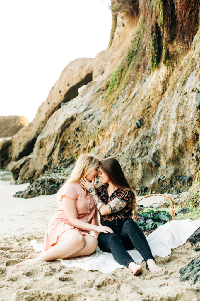 LGBTQ+ wedding photographer in san diego; a lesbian couple about to kiss, they are sitting on the sand at the beach having a picnic