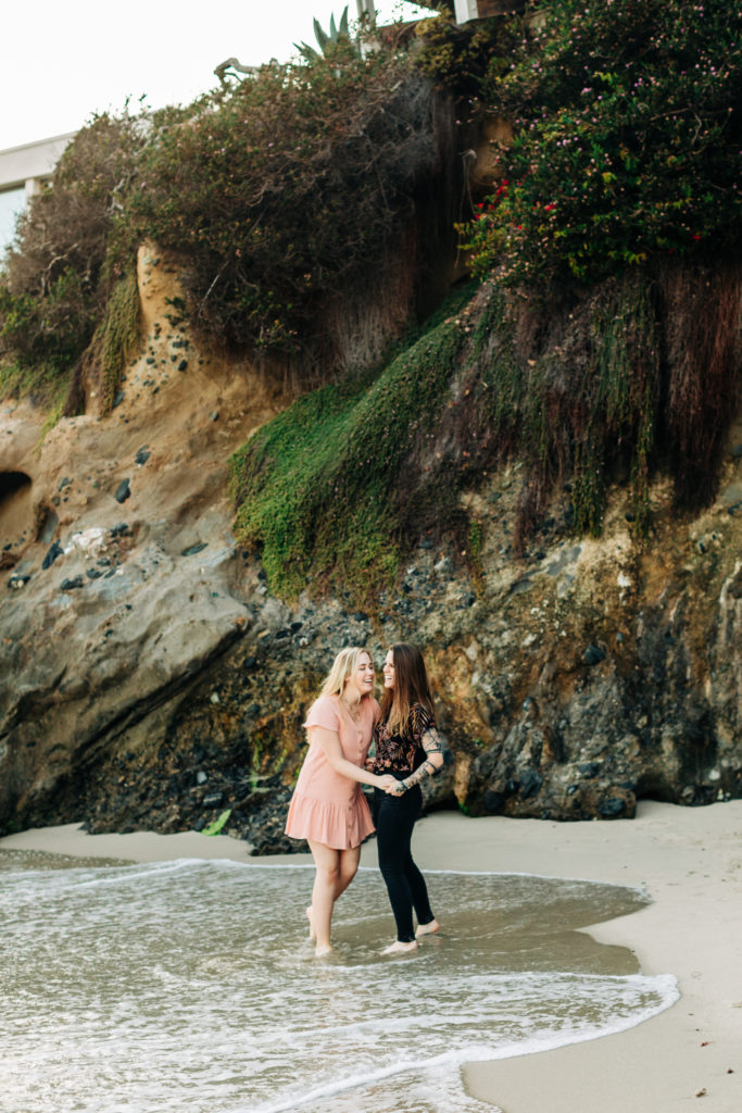LGBTQ+ wedding photographer in san diego; a lesbian couple holding hands and laughing at the beach