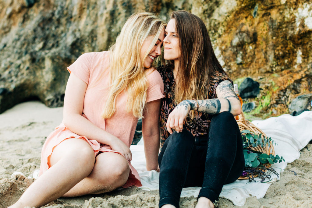 LGBTQ+ wedding photographer in san diego; a lesbian couple sitting at the beach with their heads close together