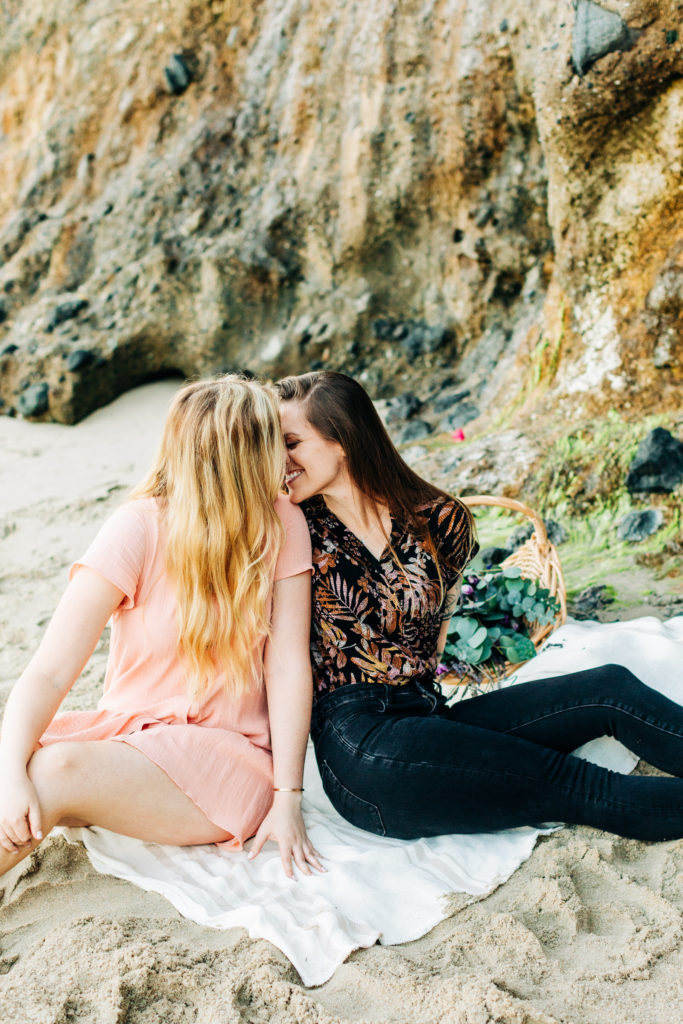 LGBTQ+ wedding photographer in san diego; a lesbian couple kissing as they sit on the sand at the beach