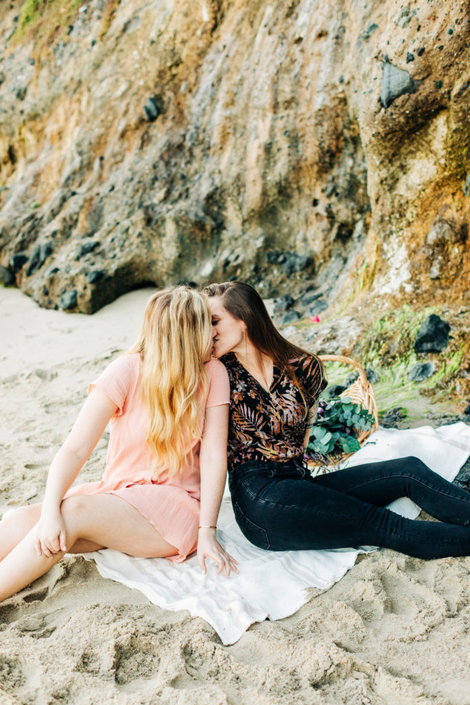 LGBTQ+ wedding photographer in san diego; two women kissing while they sit on the sand at the beach