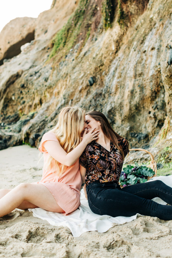 LGBTQ+ wedding photographer in san diego; a lesbian couple sitting next to each other on the beach having a picnic, they are kissing