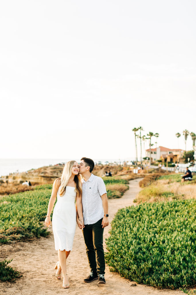 san diego engagement photos at sunset cliffs; san diego wedding photographer; a man and woman walking, the man kisses the woman on the cheek