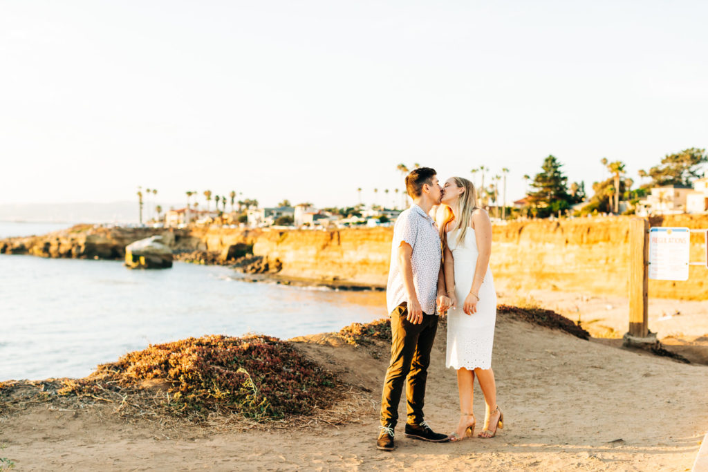 san diego engagement photos at sunset cliffs; san diego wedding photographer; a man and woman are kissing each other while standing on sunset cliffs in san diego