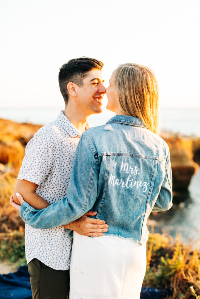 san diego engagement photos at sunset cliffs; san diego wedding photographer; a woman wearing a jean jacket is about to kiss her boyfriend