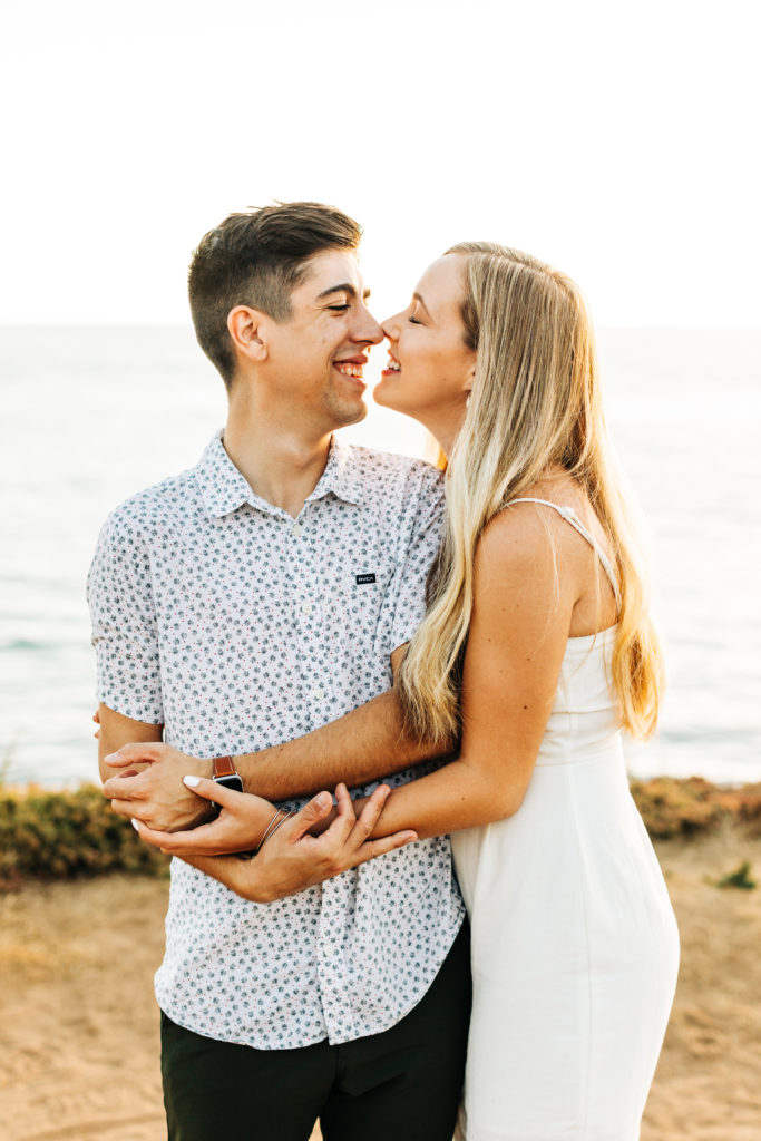 san diego engagement photos at sunset cliffs; san diego wedding photographer; a woman and a man about to kiss, they are smiling and hugging