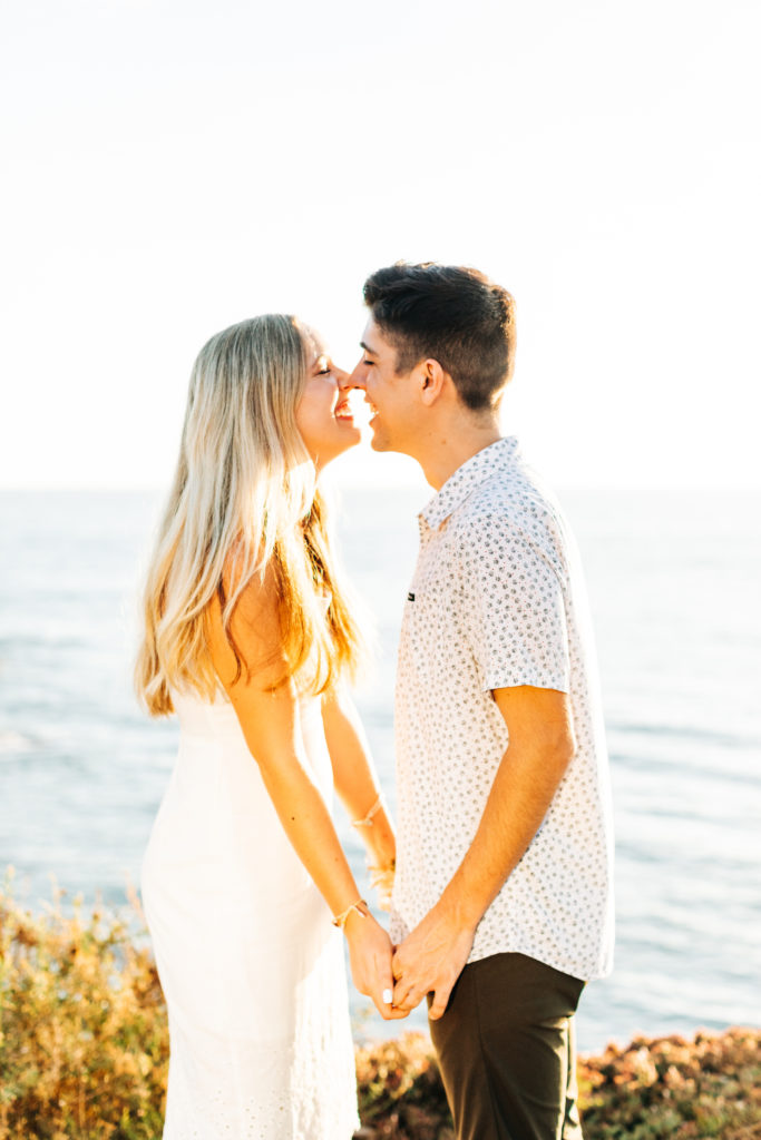 san diego engagement photos at sunset cliffs; san diego wedding photographer; a man and woman facing each other, they are holding hands and smiling and are about to kiss, the ocean is in the background