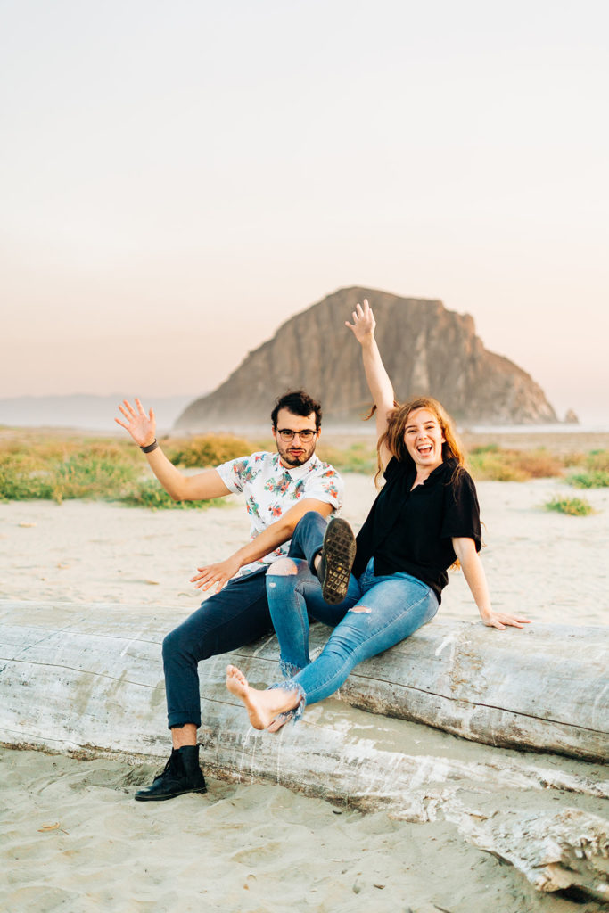 Sunset Engagement Photos at Morro Bay, morro bay wedding photographer; a man and woman joking around and making funny faces at the camera. they are sitting on a log at the beach
