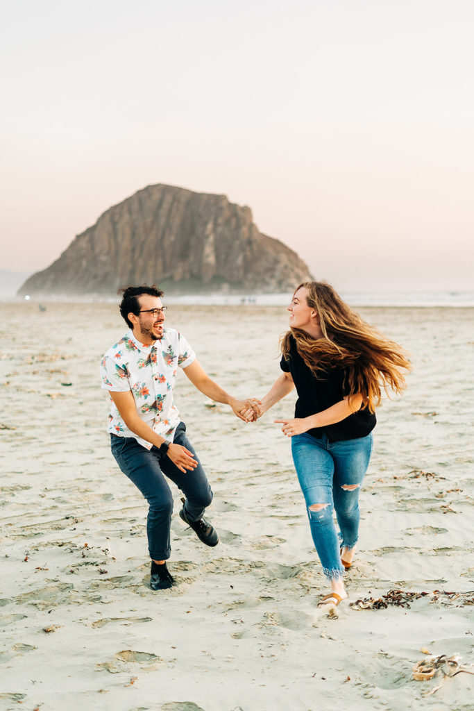 Sunset Engagement Photos at Morro Bay, morro bay wedding photographer; a man and woman holding hands and running on the beach in Morro Bay, California