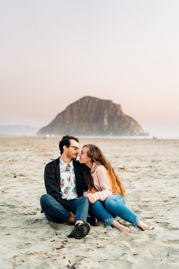 Sunset Engagement Photos at Morro Bay, morro bay wedding photographer; a man and woman sitting close together on the beach in morro bay, california; a couple about to kiss on the beach