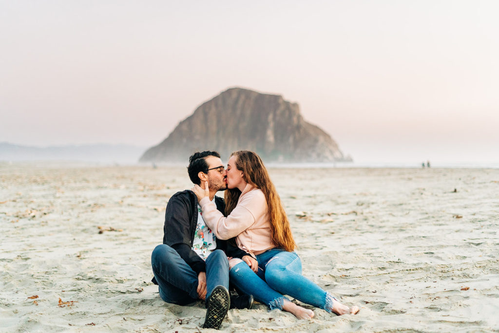 Sunset Engagement Photos at Morro Bay, morro bay wedding photographer; a couple kissing on the beach in morro bay, california as they sit on the sand