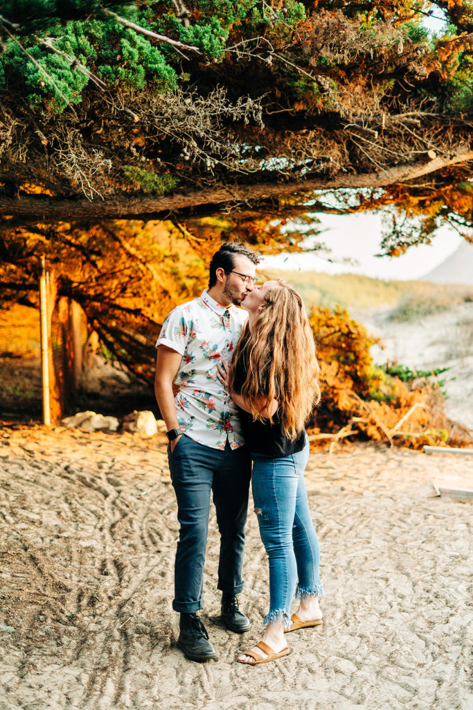 Sunset Engagement Photos at Morro Bay, morro bay wedding photographer; a man and woman couple kissing on the beach, they are walking under trees