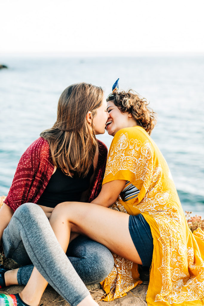 san diego wedding photographer; sunset cliffs engagement photos; two women about to kiss each other at sunset cliffs in san diego, california. they are sitting on the ground on a cliff overlooking the ocean.