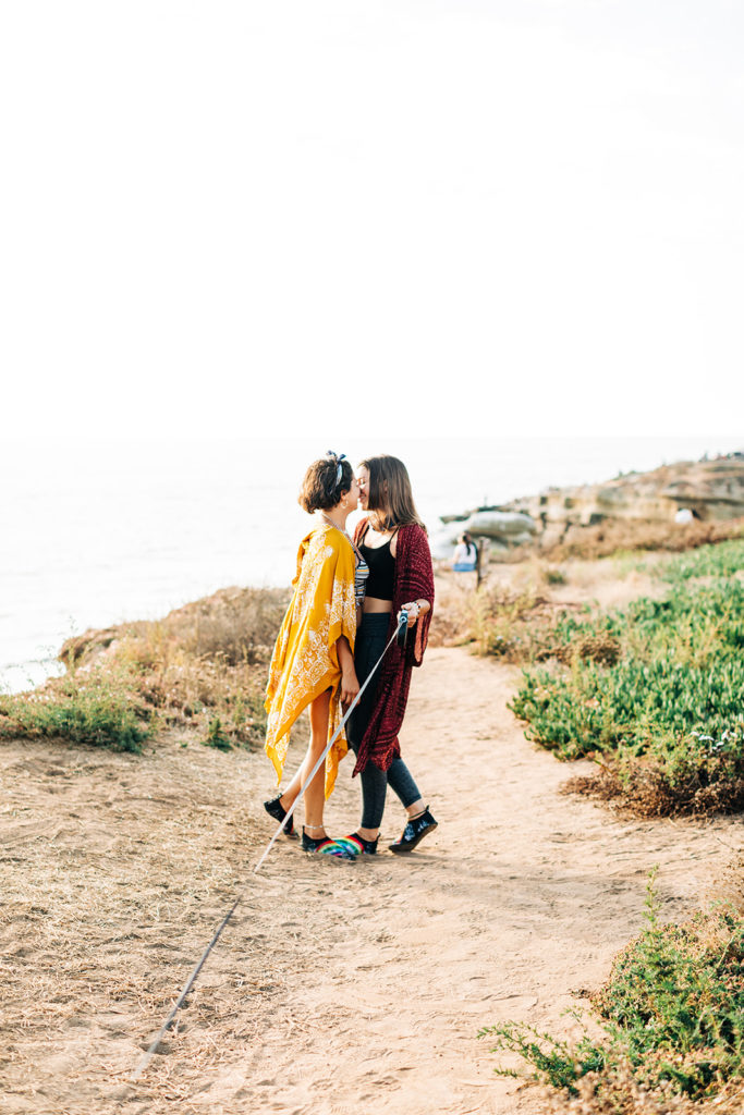 san diego wedding photographer; sunset cliffs engagement photos; a lesbian couple kissing while walking their dog at sunset cliffs in san diego, california