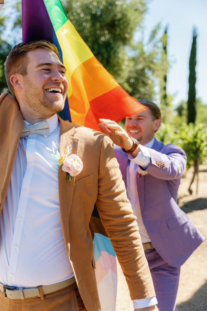 two grooms running with a pride flag on their wedding day; gay wedding in temecula at mount palomar winery