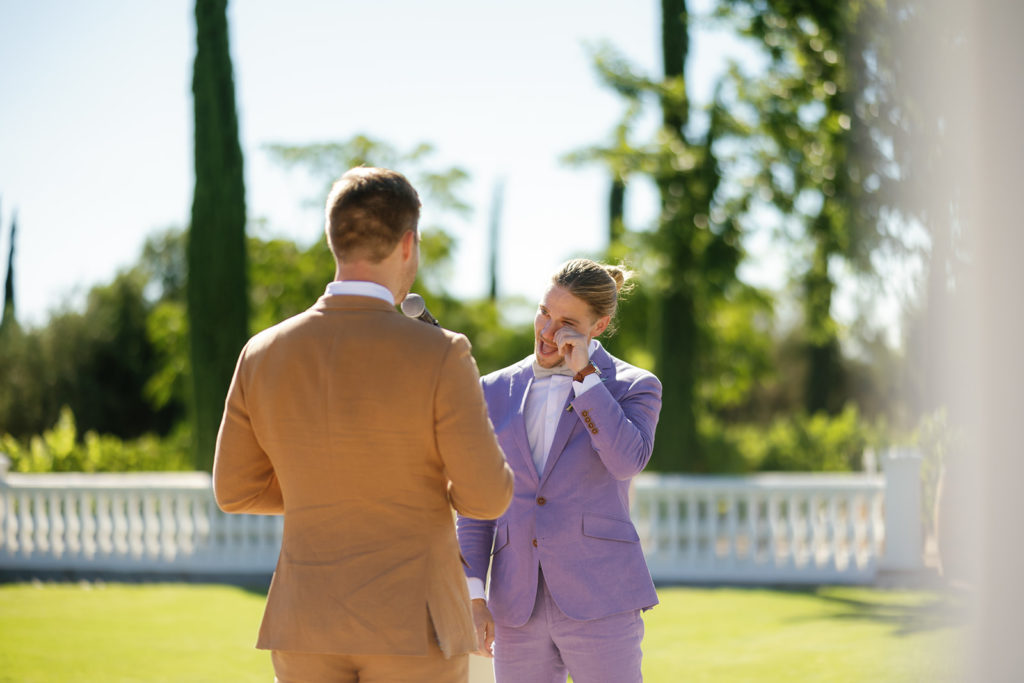 A groom wipes his tears as his groom reads his vows to him at their wedding; gay wedding in temecula at mount palomar winery