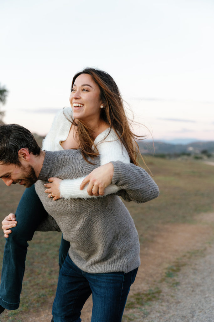 Romantic San Diego Engagement Photos; a man playfully throws his fiancee over his shoulder during their engagement photo session.
