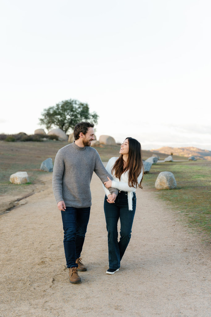 Romantic San Diego Engagement Photos; a man and woman walking and smiling at each other during their engagement photo session.
