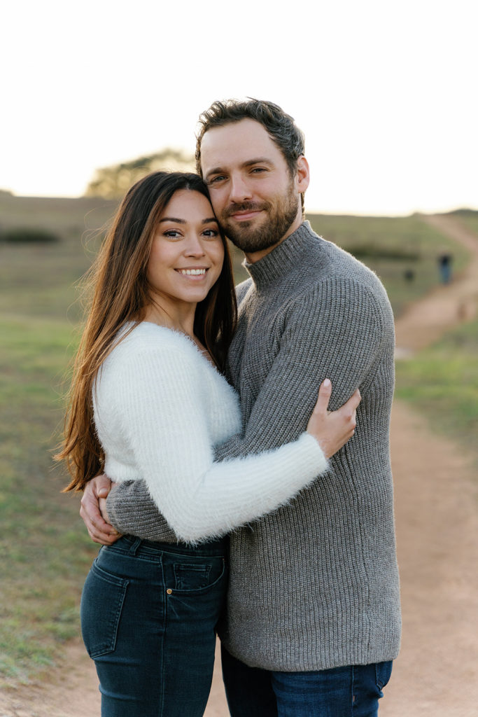 Romantic San Diego Engagement Photos; a man and woman smiling at the camera as they hug during their engagement photo session.