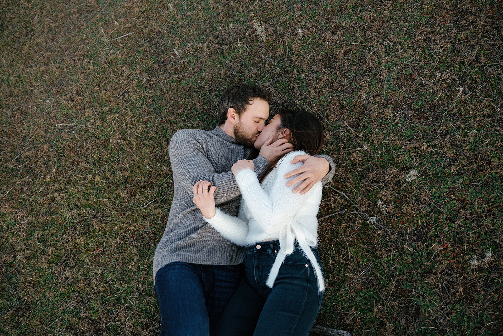Romantic San Diego Engagement Photos; a man and woman laying down and kissing on the grass during their engagement photo session.