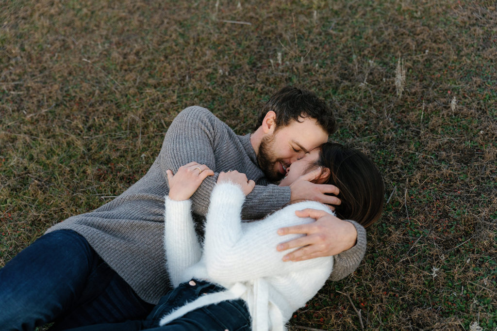 Romantic San Diego Engagement Photos; a man and woman laying down cuddling on the grass during their engagement photo session.