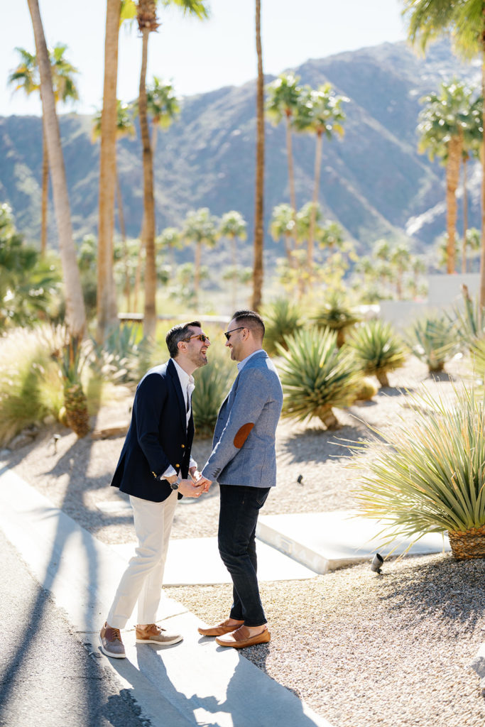 palm springs engagement photos; a gay couple holding hands and smiling at each other
