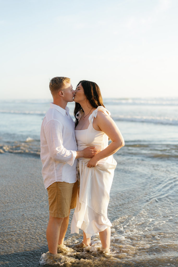 a couple kissing in the water at their engagement session at del mar dog beach in san diego