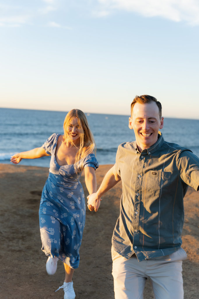 san diego wedding photographer; a couple runs toward the camera during their engagement session at sunset cliffs in san diego