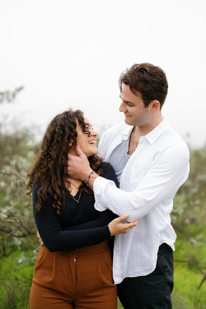romantic san diego engagement photos; romantic location for engagement photos in san diego; a man touching his girlfriends face lovingly, they are looking at each other