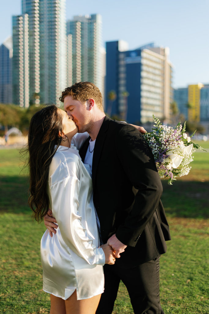 waterfront park engagement photos in san diego; a couple kisses during their engagement session in front of buildings