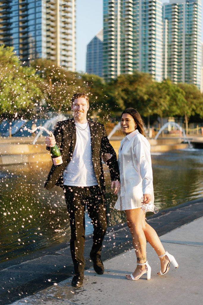 waterfront park engagement photos in san diego; a man and woman pop champagne during their engagement session at waterfront park in san diego at golden hour