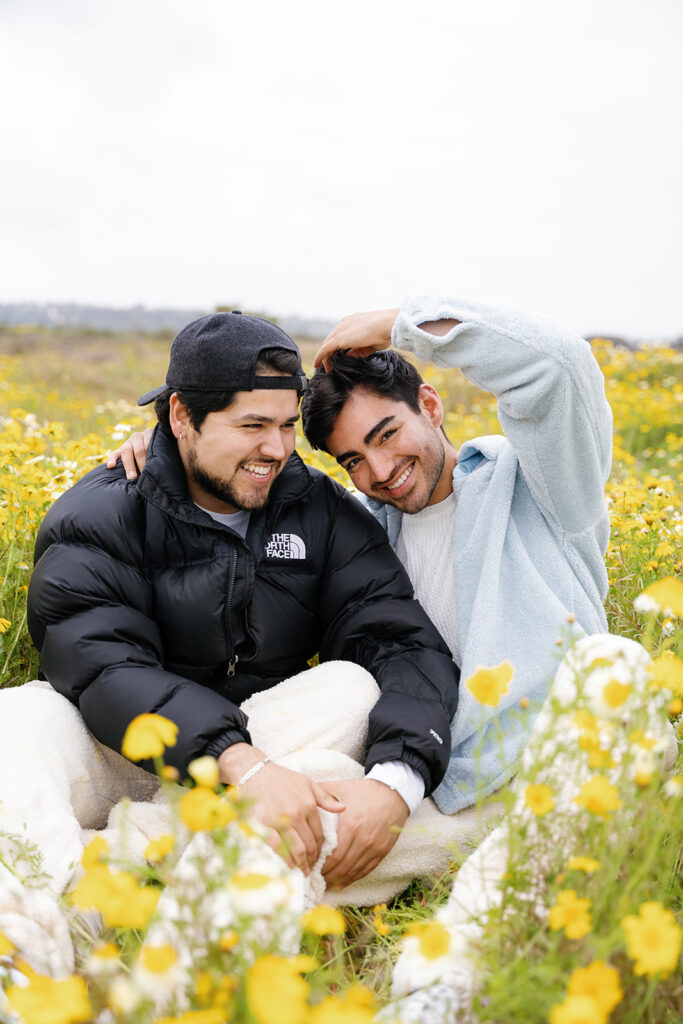 wildflowers superbloom in san diego; a gay couple sitting together in a field of wildflowers in san diego, they are smiling