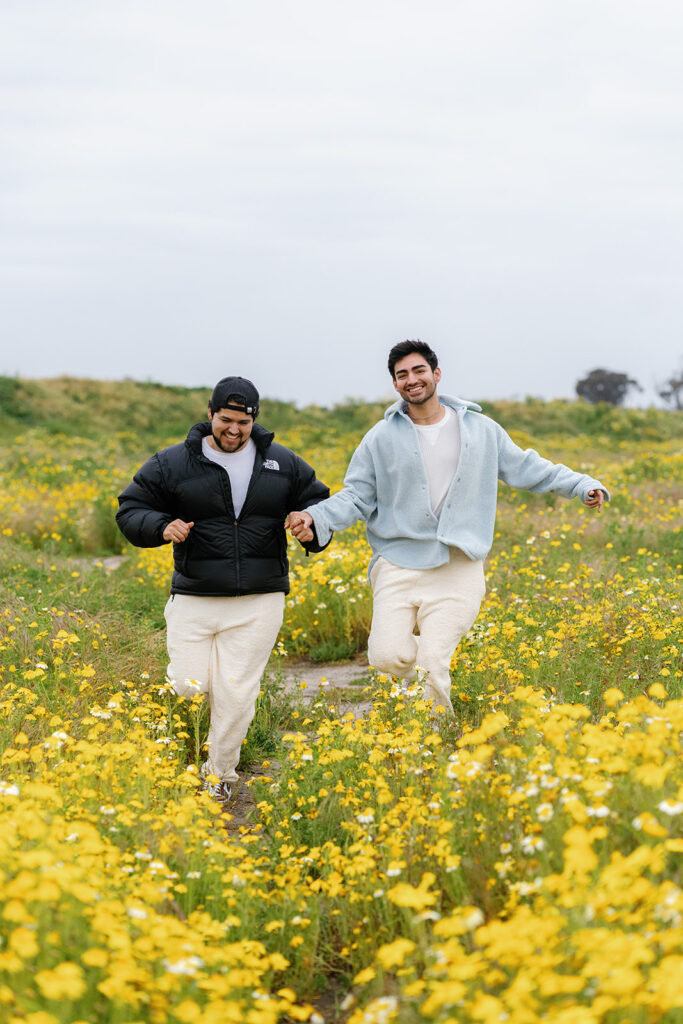 wildflowers superbloom in san diego; an lgbtq+ couple holding hands and running towards the camera in a field of wildflowers in san diego